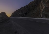 a lone road with a mountain in the background and seagull flying over the ocean