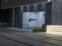 the entrance to a building at night with lights on a pathway that leads to an open door