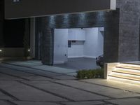 the entrance to a building at night with lights on a pathway that leads to an open door