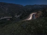 a winding road and a hillside at night with lights on the sides of the hills