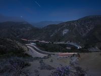 a long exposure photograph of the highway in the mountains at night with the stars above them