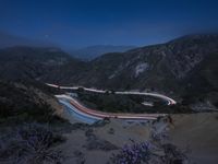 a long exposure photograph of the highway in the mountains at night with the stars above them