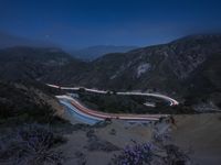 a long exposure photograph of the highway in the mountains at night with the stars above them