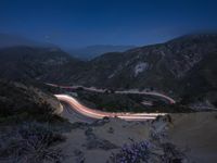 a long exposure photograph of the highway in the mountains at night with the stars above them