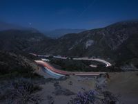 a long exposure photograph of the highway in the mountains at night with the stars above them