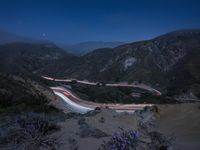 a long exposure photograph of the highway in the mountains at night with the stars above them