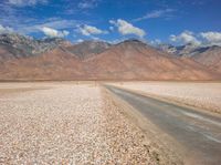 a lone road running through a barren field with mountains in the background on a sunny day