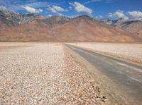 a lone road running through a barren field with mountains in the background on a sunny day