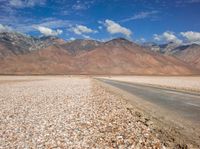 a lone road running through a barren field with mountains in the background on a sunny day