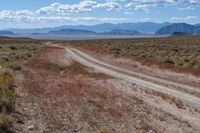 a dirt road passing through the desert under a partly cloudy sky with mountains behind it