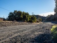 an empty dirt road with green brush and bushes in the background, and blue sky above