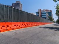 a long road lined with orange barrier and a building in the background of a fence