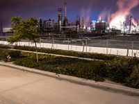 a view looking down at an oil refinery and street lights from a sidewalk area at night