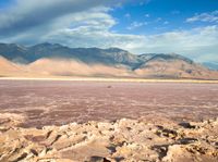 a man sitting on some rocks in the desert with mountains and water behind him in front of them