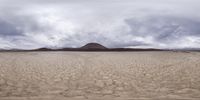 an open sandy field with sand in it with the sky and a mountain behind it