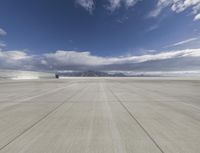 a concrete runway under a partly cloudy sky in an empty desert area in the mountains