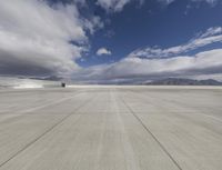 a concrete runway under a partly cloudy sky in an empty desert area in the mountains