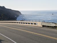 a motorcycle traveling on a road next to the ocean overpassed with traffic barriers