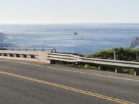 a motorcycle traveling on a road next to the ocean overpassed with traffic barriers