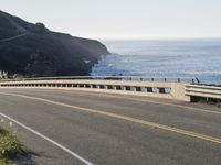a motorcycle traveling on a road next to the ocean overpassed with traffic barriers