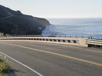 a motorcycle traveling on a road next to the ocean overpassed with traffic barriers