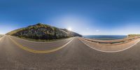 road in front of mountains and a sunny sky with sun and sunburst above them