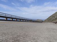 a highway with a metal bridge and the ocean beyond it with green grass and rocks