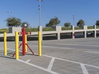 a red fire hydrant is positioned behind yellow poles in a parking lot under a blue sky