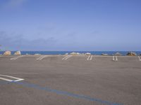 empty parking lot with blue and white markings on the ground next to the ocean and rocks