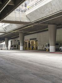 an empty parking lot surrounded by tall concrete pillars with the doors opened and cars outside