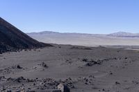 a rocky landscape with boulders and desert mountains in the distance, with a blue sky