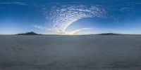 a panoramic shot of a plain with an almost cloudy sky and mountains in the background