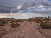 a dirt road in the middle of an arid area under clouds and sun set over mountains