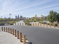 a view of a road with wooden posts and people walking past it with cityscape in the background