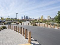 a view of a road with wooden posts and people walking past it with cityscape in the background