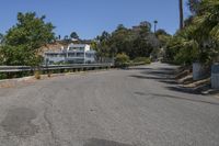 an empty road runs past a large white building in the distance, surrounded by trees and shrubs