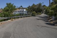 an empty road runs past a large white building in the distance, surrounded by trees and shrubs