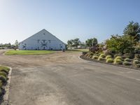 a farm and barn with lots of plants outside and the driveway next to it to the barn