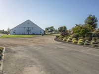 a farm and barn with lots of plants outside and the driveway next to it to the barn