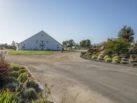 a farm and barn with lots of plants outside and the driveway next to it to the barn