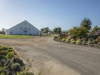 a farm and barn with lots of plants outside and the driveway next to it to the barn