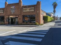 a brick building sits on the corner of an empty street with crosswalks and palm trees