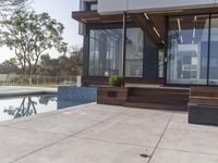 a glass walled outdoor patio overlooking a pool with wooden benches and a fire pit, on the corner of a house