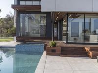 a glass walled outdoor patio overlooking a pool with wooden benches and a fire pit, on the corner of a house