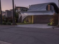 a modern home with a curved roof and exterior in the evening sun light, sitting in a driveway between palm trees