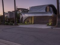 a modern home with a curved roof and exterior in the evening sun light, sitting in a driveway between palm trees