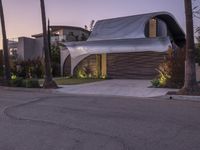 a modern home with a curved roof and exterior in the evening sun light, sitting in a driveway between palm trees