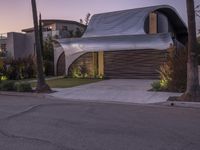 a modern home with a curved roof and exterior in the evening sun light, sitting in a driveway between palm trees