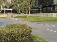 a black car is traveling down the street near tall buildings, a parking area with plants and bushes