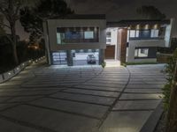 two house that are lit up at night in front of the driveway with lights on